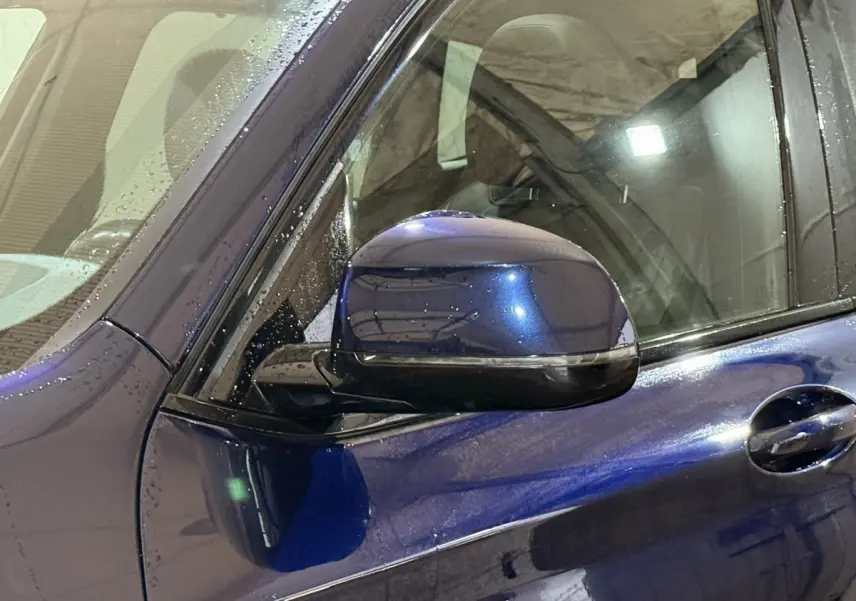 Rétroviseur côté gauche bleu métallisé d'un BMW X3 xDrive30e 2023, avec poignée de porte et vitre partielle visible.