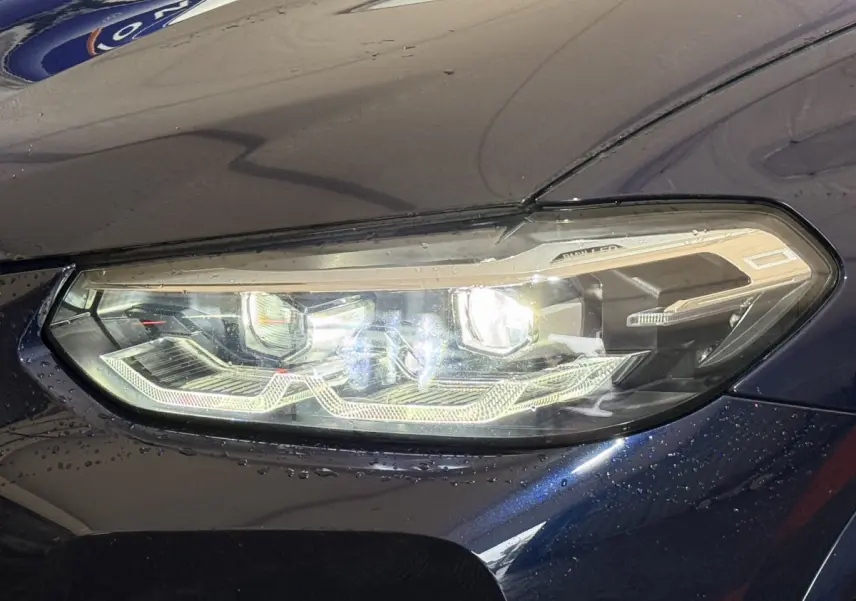 Gros plan sur le phare avant droit allumé d'un BMW X3 xDrive30e bleu 2023 avec détails LED distinctifs.