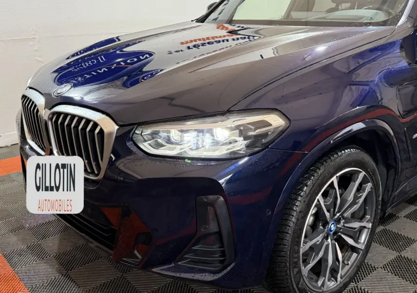Vue 3/4 avant droit d'un BMW X3 xDrive30e bleu avec phares LED allumés et jantes alliage distinctives.