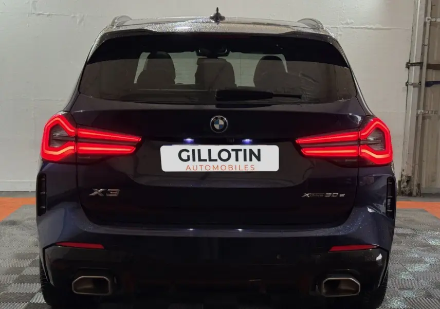 Vue arrière d'un BMW X3 xDrive30e bleu 2023 avec feux LED allumés et double sortie d'échappement rectangulaire.