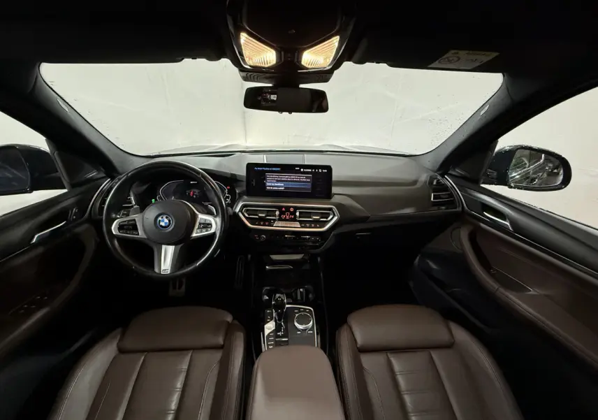 Vue intérieure avant du BMW X3 xDrive30e 2023 avec tableau de bord moderne et sièges en cuir marron.