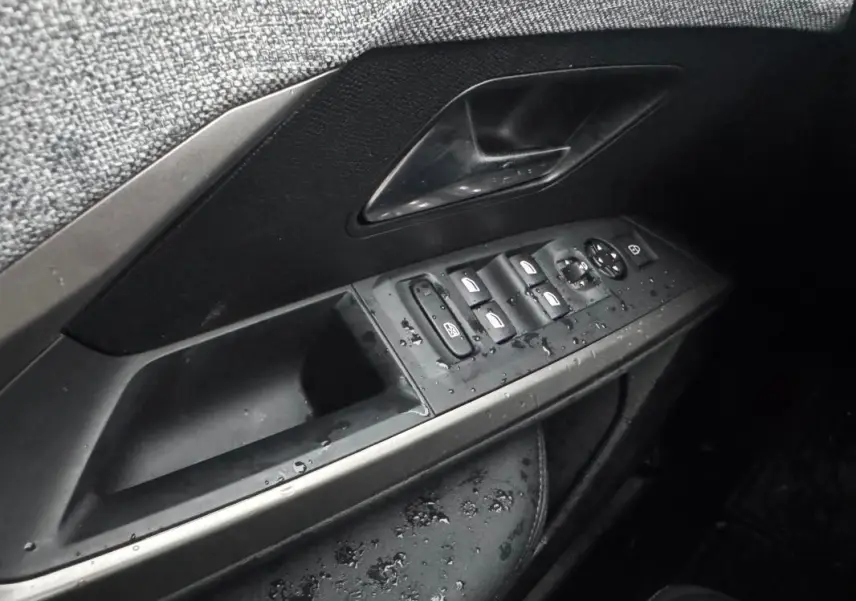 Gros plan sur la commande des vitres et rétroviseurs côté conducteur du Peugeot 3008 Hybrid noir, intérieur humide.
