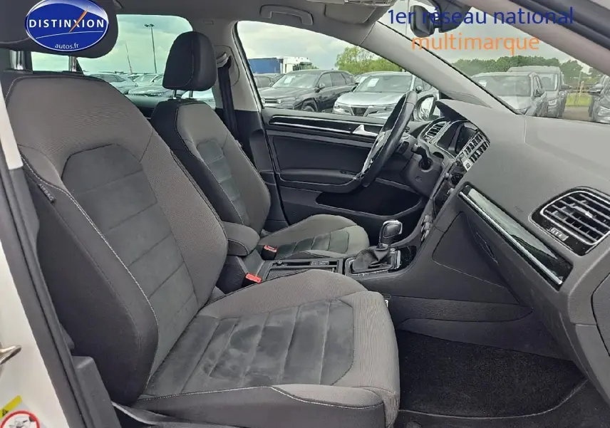 Vue intérieure côté conducteur de la Volkswagen Golf blanche, montrant les sièges tissu gris et le tableau de bord.