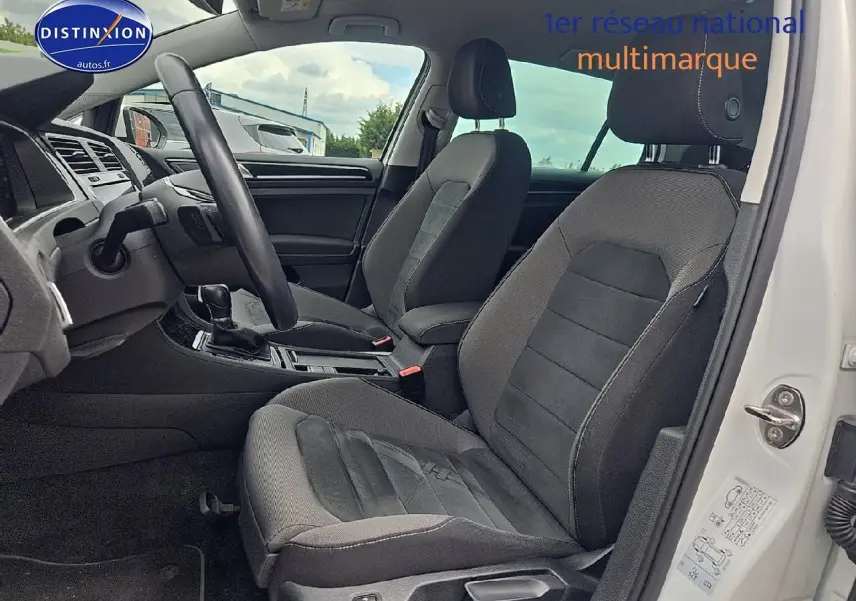 Vue intérieure côté conducteur de la Volkswagen Golf blanche 2019, montrant les sièges avant en tissu gris et la console centrale.