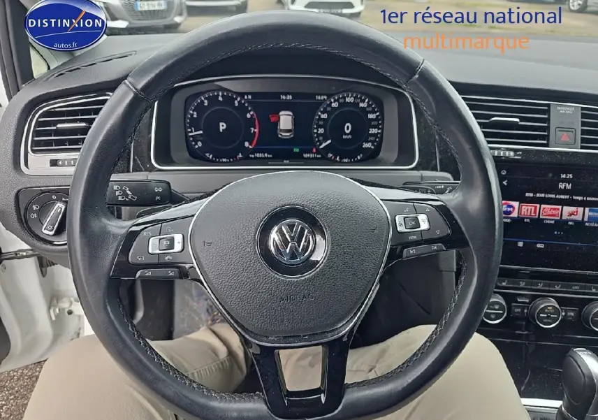 Vue intérieure centrée sur le volant cuir noir d'une Volkswagen Golf blanche, avec tableau de bord digital et écran tactile visible.