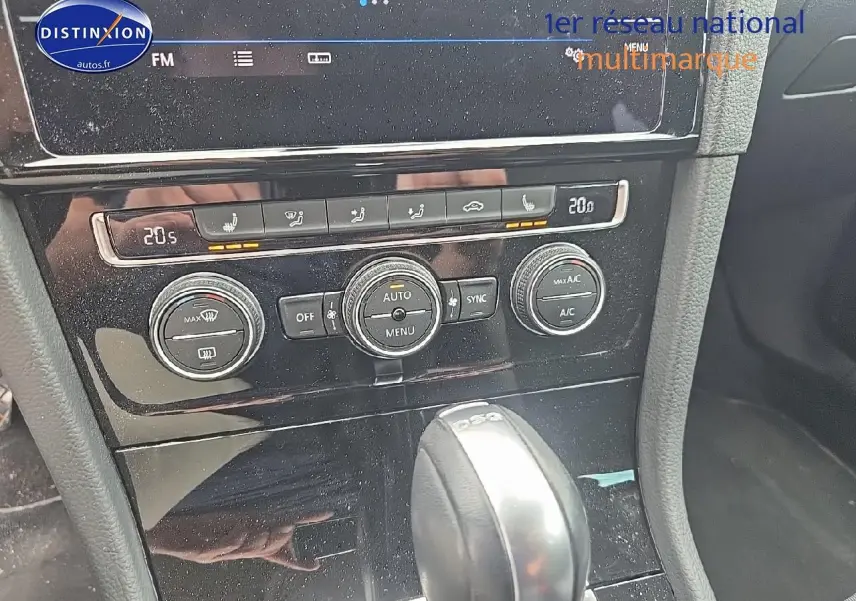 Vue rapprochée de la console centrale noire avec commandes climatisation et levier de vitesse DSG d’une Volkswagen Golf blanche.