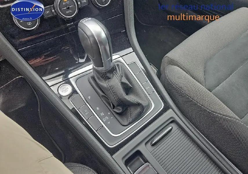 Gros plan sur la console centrale avec levier de boîte auto et siège tissu gris côté droit d’une Volkswagen Golf blanche.