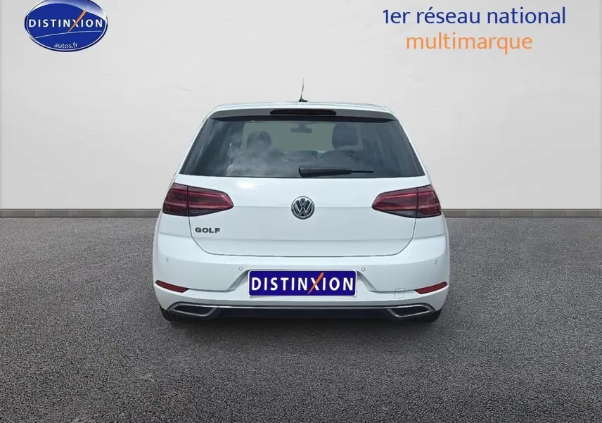 Vue arrière d'une Volkswagen Golf blanche garée sur un sol gris, avec feux arrière LED visibles.