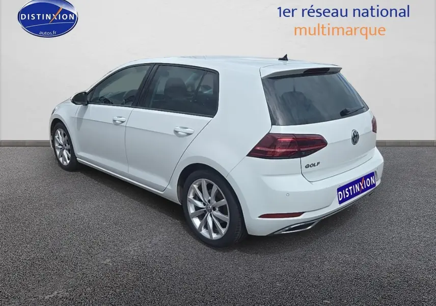 Vue 3/4 arrière droite d'une Volkswagen Golf blanche avec jantes alu et vitres teintées sur fond neutre.