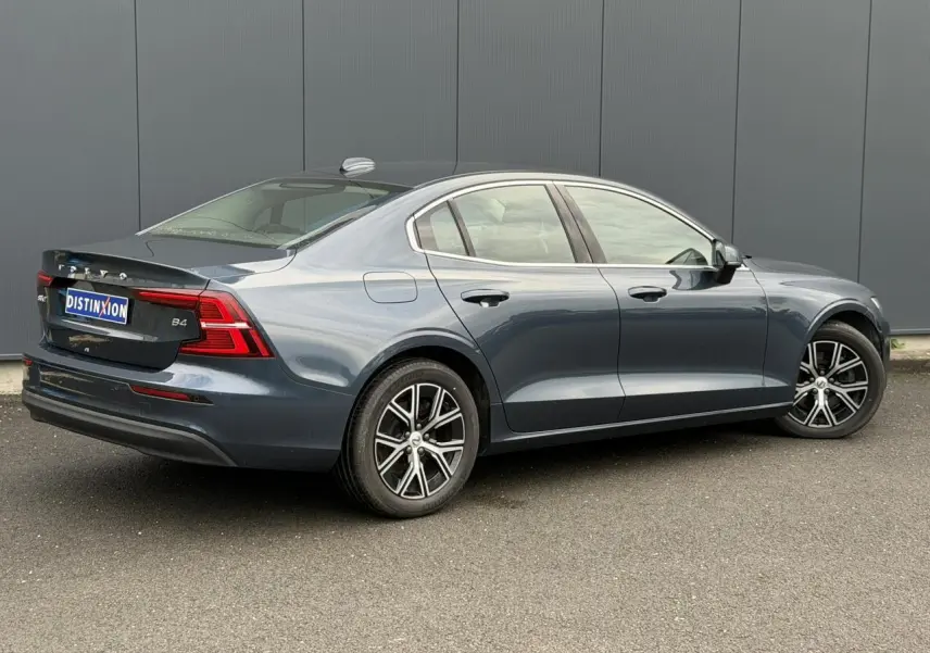 Vue 3/4 arrière côté droit d'une Volvo S60 B4 197 DCT7 MHEV Core+ gris Denim avec jantes alliage 17 pouces.