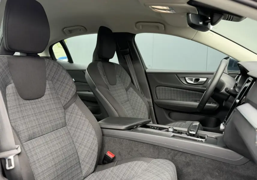 Vue intérieure côté droit de la Volvo S60 2024, sièges tissu gris à motif écossais avec console centrale et volant visibles.