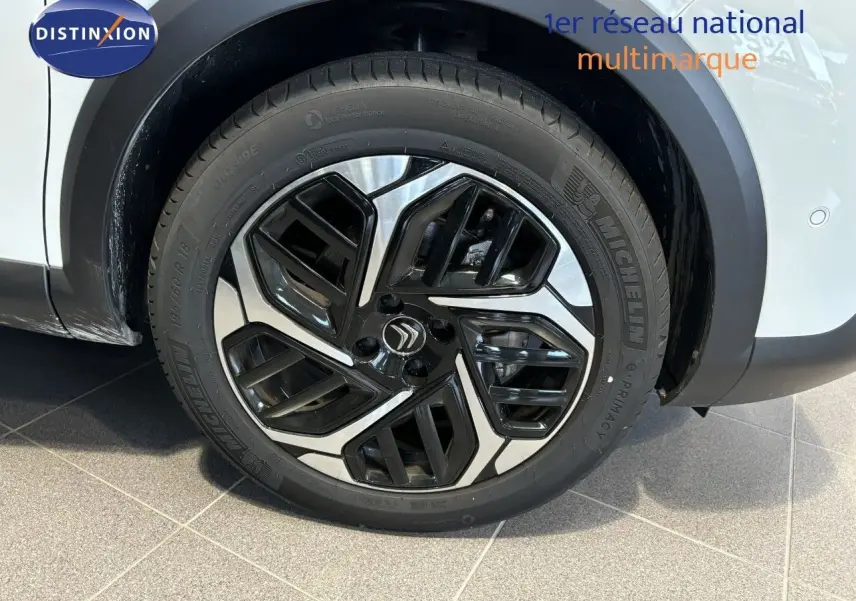 Gros plan sur la roue avant droite d'une Citroën C4 blanche 2022, mettant en valeur la jante noire et argentée au design moderne.