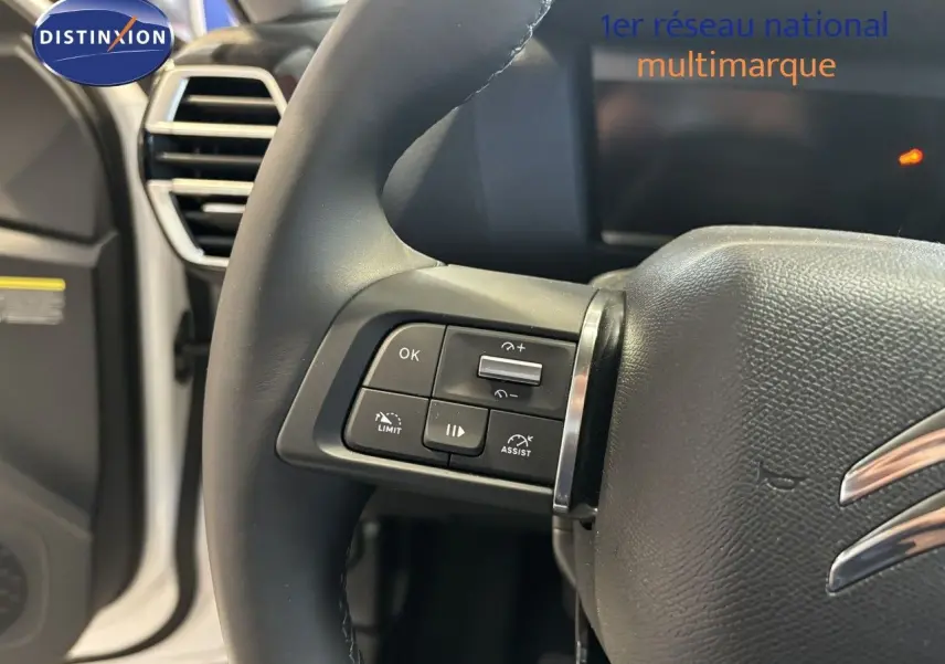 Gros plan sur le volant multifonction noir de la Citroën C4 blanche, mettant en valeur les commandes de régulateur et limiteur de vitesse.