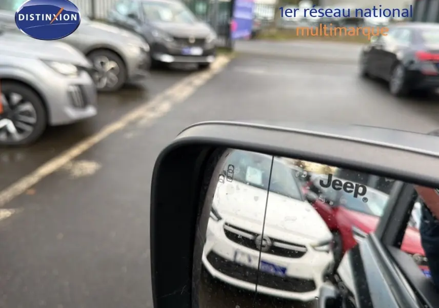 Rétroviseur latéral droit montrant la face avant blanche d'un Jeep Renegade en stationnement.