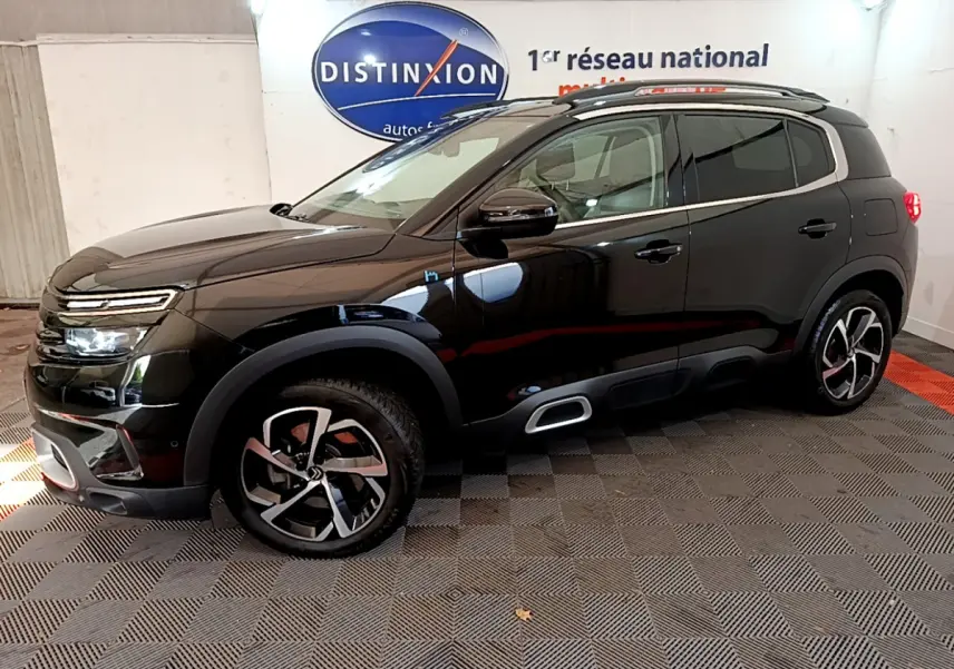 Vue de profil côté gauche d'un Citroën C5 Aircross Hybrid noir avec jantes alliage et barres de toit chromées.
