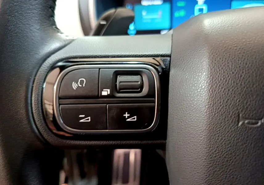 Gros plan sur les commandes gauche du volant cuir du Citroën C5 Aircross Hybrid noir, avec affichage digital en arrière-plan.