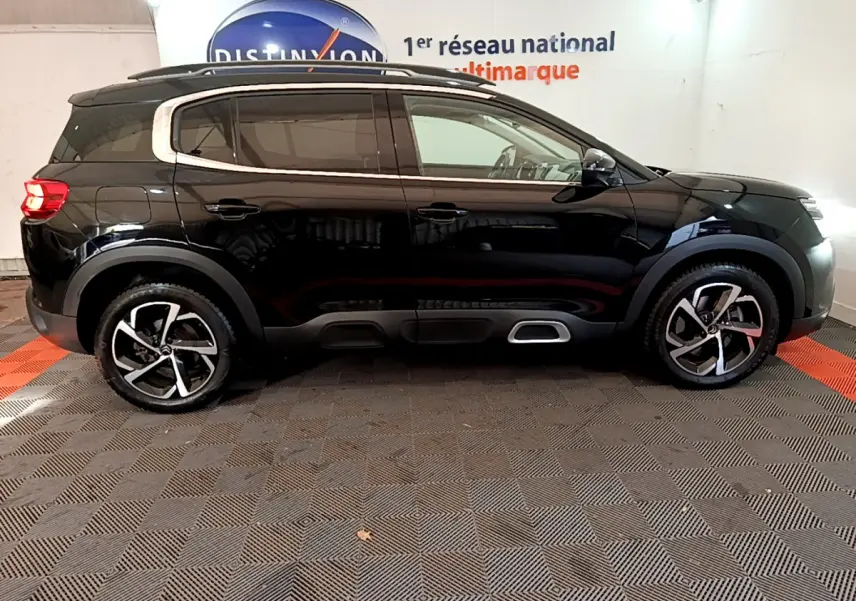 Profil côté droit d'un Citroën C5 Aircross Hybrid 225 noir, avec jantes alliage et barres de toit chromées visibles.