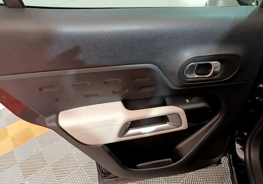 Gros plan sur la garniture intérieure de la porte côté gauche du Citroën C5 Aircross Hybrid noir, avec accoudoir clair et poignée chromée.