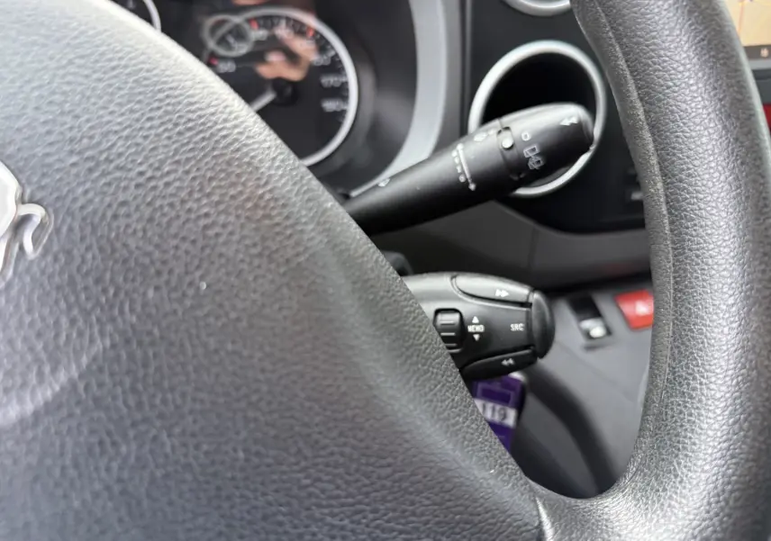 Gros plan sur le volant noir et les commandes au volant du Peugeot Partner Tepee 1.6 HDI 2018, intérieur gris.