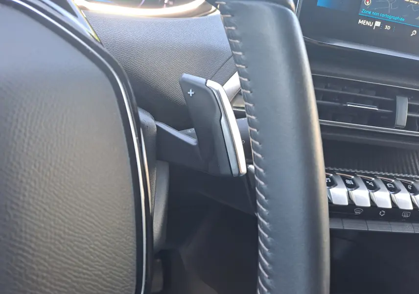 Gros plan sur la palette de changement de vitesse droite du volant cuir noir du Peugeot 3008 2023, avec tableau de bord et écran tactile visibles.
