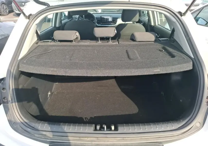 Coffre ouvert vu de l'arrière d'un KIA STONIC blanc 2023, avec cache-bagages et sièges arrière visibles.