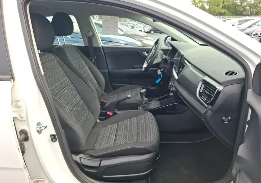 Vue intérieure côté conducteur du Kia Stonic blanc 2023, montrant les sièges avant et la console centrale avec boîte manuelle.