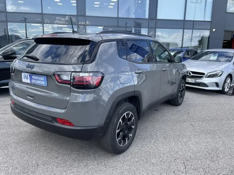 Vue 3/4 arrière droite d'un Jeep Compass gris 2023 hybride rechargeable avec jantes noires et toit noir brillant.