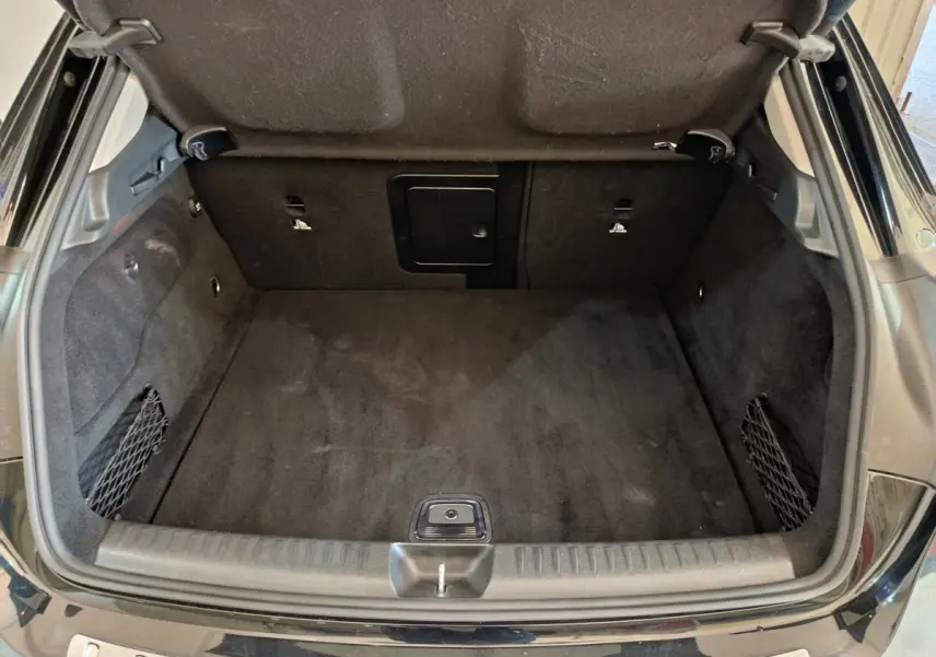 Coffre ouvert vu de l'arrière d'une Mercedes GLA 220 d Business Exec noir, tapis et parois intérieures en tissu noir.