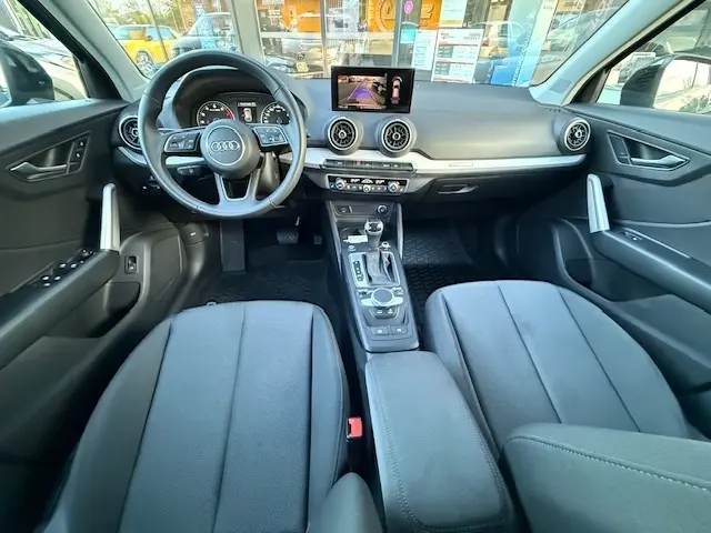 Vue intérieure avant de l'Audi Q2 35 TFSI S Line 2023 noire, avec tableau de bord numérique et écran tactile central.