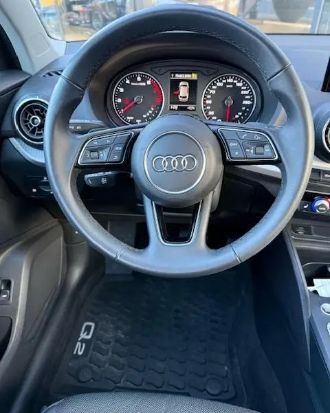 Vue intérieure centrée sur le volant cuir multifonctions de l'Audi Q2 35 TFSI noir avec tableau de bord digital.
