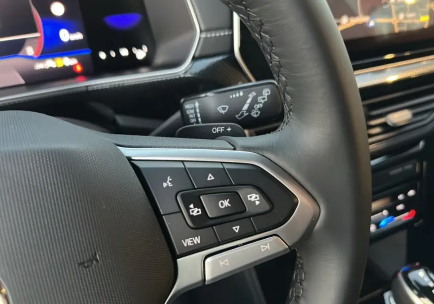 Gros plan sur le volant cuir multifonctions du Volkswagen T-Cross gris cendré, avec commandes intégrées et tableau de bord digital.