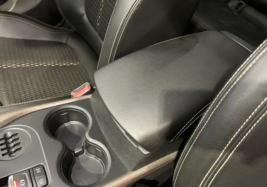 Gros plan sur la console centrale noire avec accoudoir en cuir et porte-gobelets du Renault Kadjar gris, version Intens 2015.