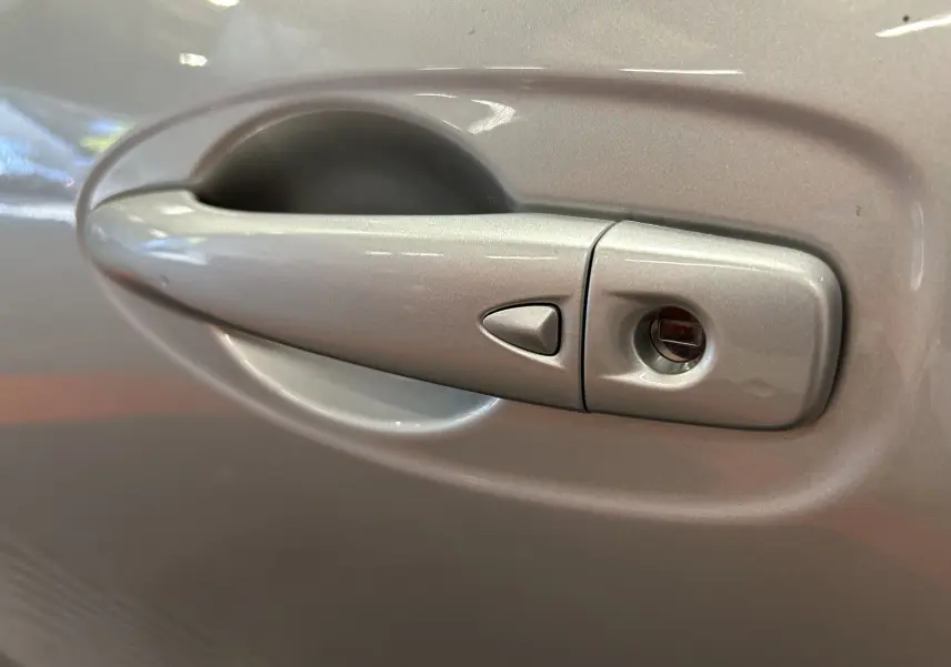 Poignée de porte gris métallisé du Renault Kadjar 2015, avec serrure intégrée et bouton triangulaire de déverrouillage.