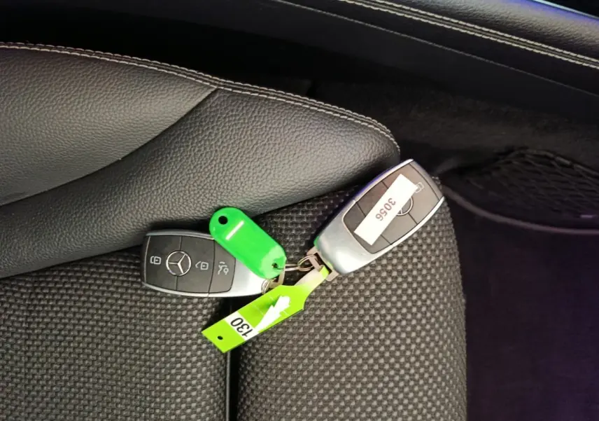Clé de voiture Mercedes GLC posée sur siège tissu noir, avec porte-clés vert et étiquette numérotée.