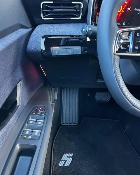 Vue intérieure côté conducteur de la Renault R5 jaune 2024, montrant les commandes de porte et le tapis noir avec logo "5".