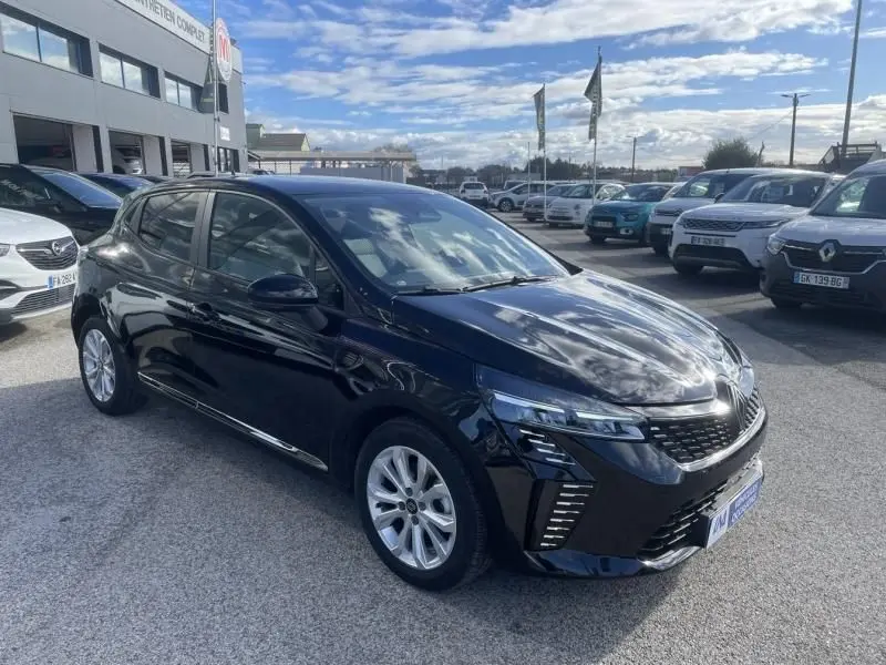 Vue 3/4 avant droite d'une Renault Clio V noire 2025, avec calandre distinctive et jantes argentées, stationnée en extérieur.