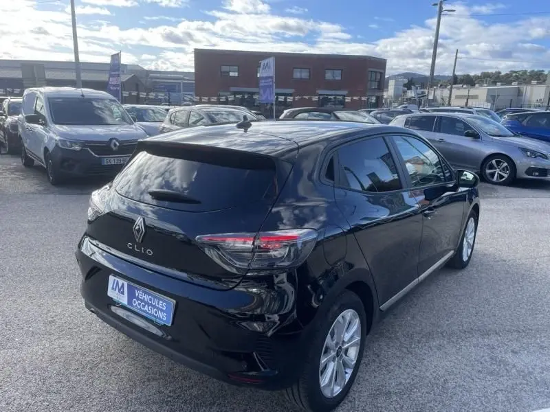 Renault Clio V noire vue 3/4 arrière droit, avec feux arrière allongés et jantes argentées, stationnée en extérieur.