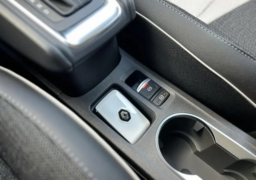Gros plan sur la console centrale noire avec bouton de frein à main électrique et porte-clés Renault gris brillant.