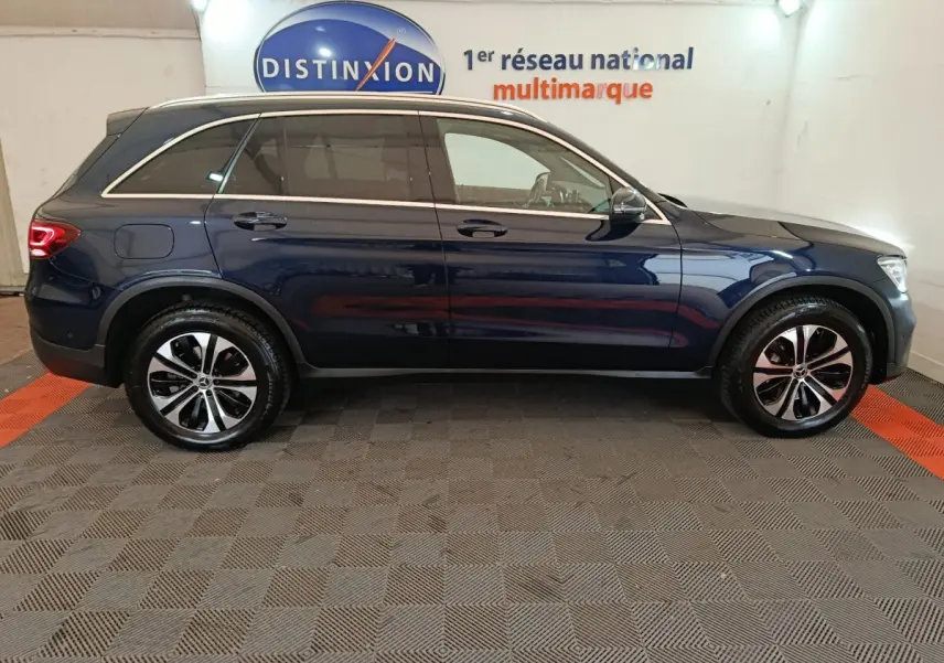 Vue latérale côté gauche d'un Mercedes GLC 300 E Business Line bleu hybride rechargeable en intérieur showroom.