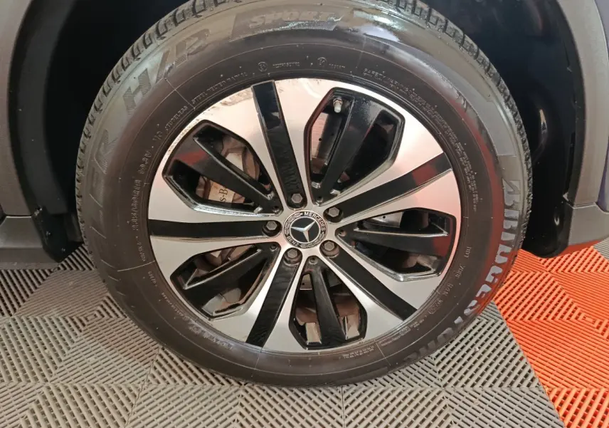 Gros plan sur la jante alliage bicolore noire et argentée d'un Mercedes GLC bleu, avec pneu Bridgestone visible.