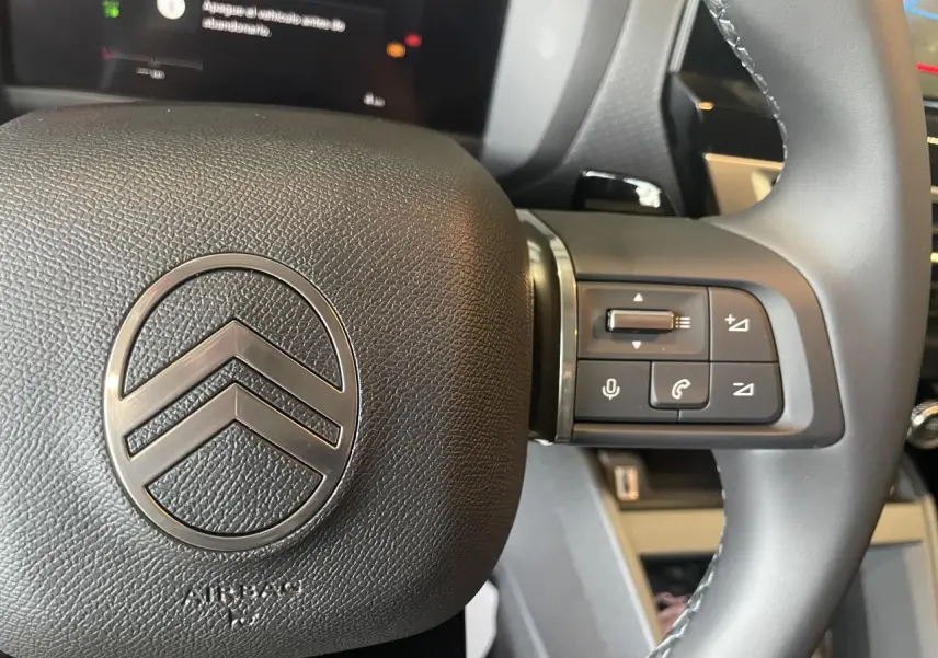 Gros plan sur le volant cuir noir de la Citroën C4 2025 avec commandes intégrées et logo chromé central.