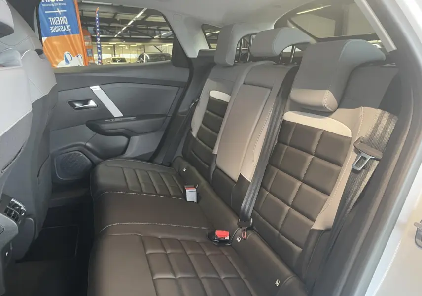 Vue latérale droite de la banquette arrière bicolore noire et beige de la Citroën C4 hybride 2025, avec ceintures et appuie-têtes.