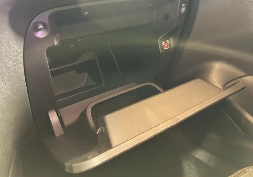 Gros plan sur la boîte à gants ouverte de l’Opel Mokka 1.2 Turbo 145 Edition noire, montrant son espace de rangement intérieur.