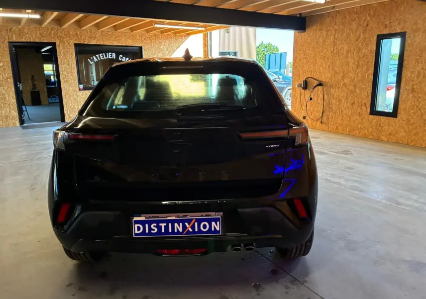 Vue arrière d'un Opel Mokka 1.2 Turbo 145 Edition noir hybride stationné dans un garage lumineux.