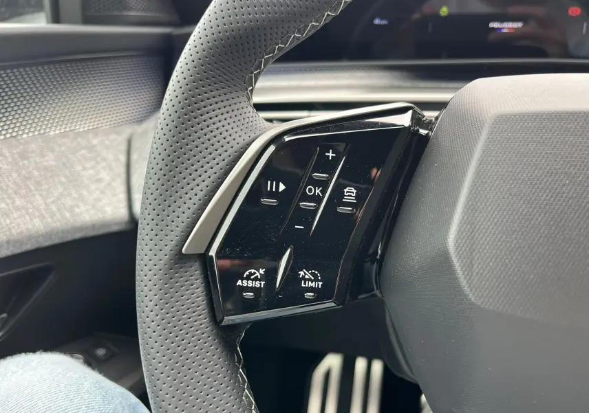 Gros plan sur les commandes du volant en cuir perforé du Peugeot 3008 Gris Titane, avec boutons d'assistance et limitation.