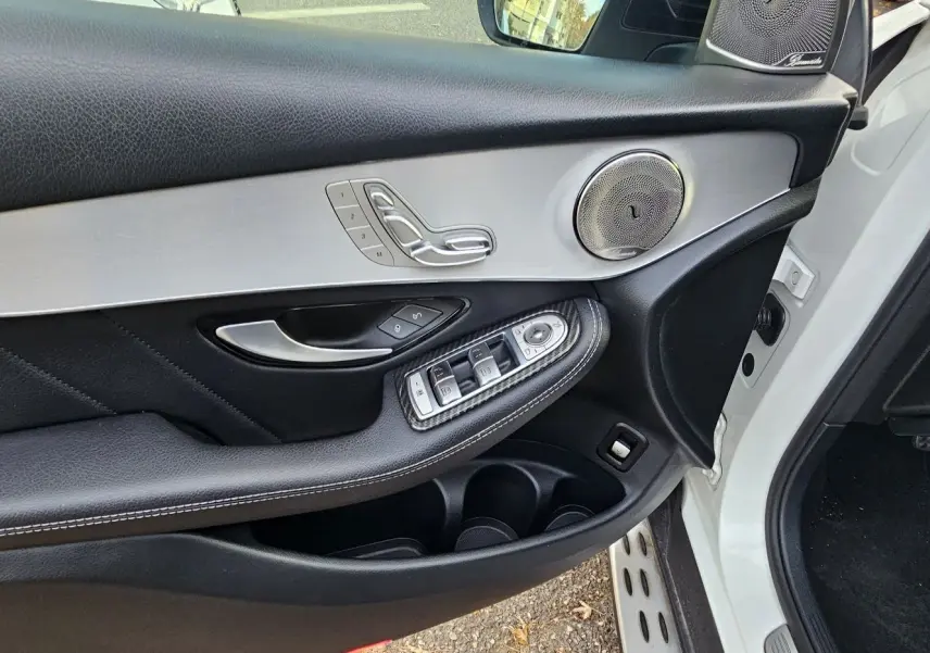 Détail de la porte avant gauche d'un Mercedes GLC Coupé blanc, avec commandes de vitres et haut-parleur argenté.
