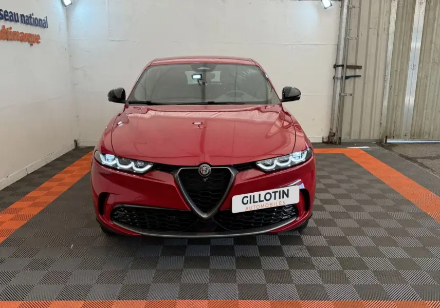 Vue frontale d'une Alfa Romeo Tonale rouge avec calandre caractéristique en V et phares LED allumés.