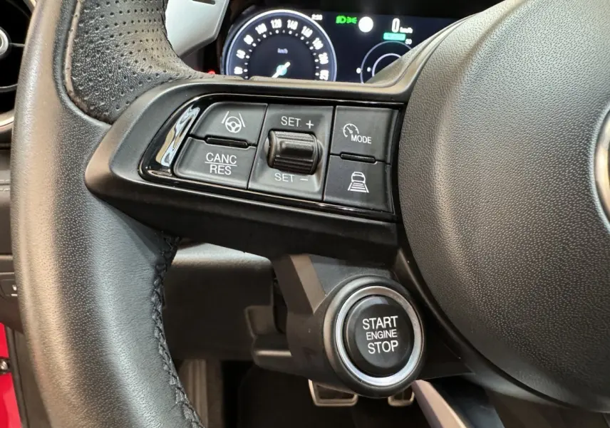 Gros plan sur le volant cuir noir de l'Alfa Romeo Tonale rouge 2023 avec commandes de régulateur et bouton start/stop visible.