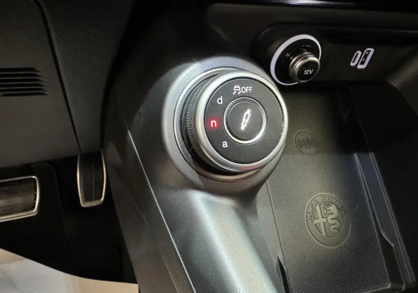 Gros plan sur la molette de sélection de boîte auto et la zone de recharge avec logo Alfa Romeo dans l'habitacle noir du Tonale.