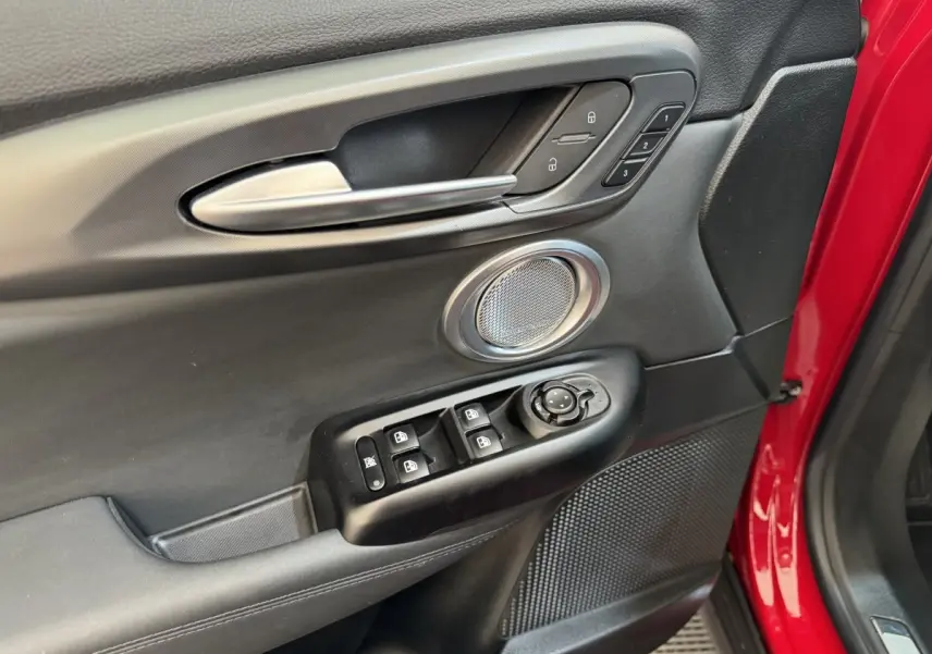 Gros plan sur la porte avant gauche rouge de l'Alfa Romeo Tonale avec commandes de vitres et haut-parleur intégré.